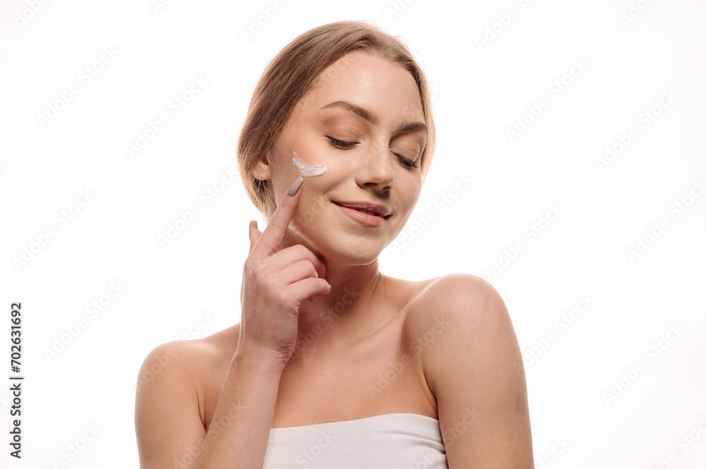 Beauty portrait of a beautiful girl applying cream on her face on an isolated white background. The concept of facial care or cosmetology Beauty portrait of a beautiful girl applying cream on her face on an isolated white background. The concept of facial care or cosmetology