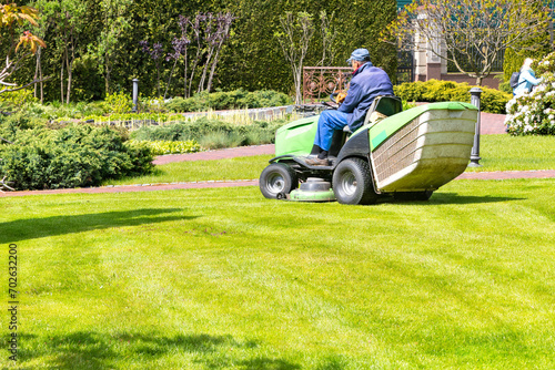 A gardener uses a tractor-type industrial lawn mower to cut the grass. Professional Gardening Details