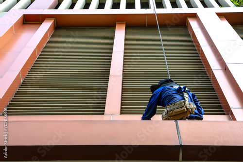Back view high rise cleaner worker with rope access cleaning fa cade windows, risk and dangerous work photo