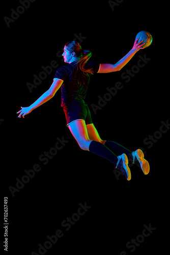 Fototapeta Naklejka Na Ścianę i Meble -  Determined woman, handball player in action, exhibiting focus and energy during training against black background in neon light. Concept of professional sport, hobby, movement, dynamic, championship.