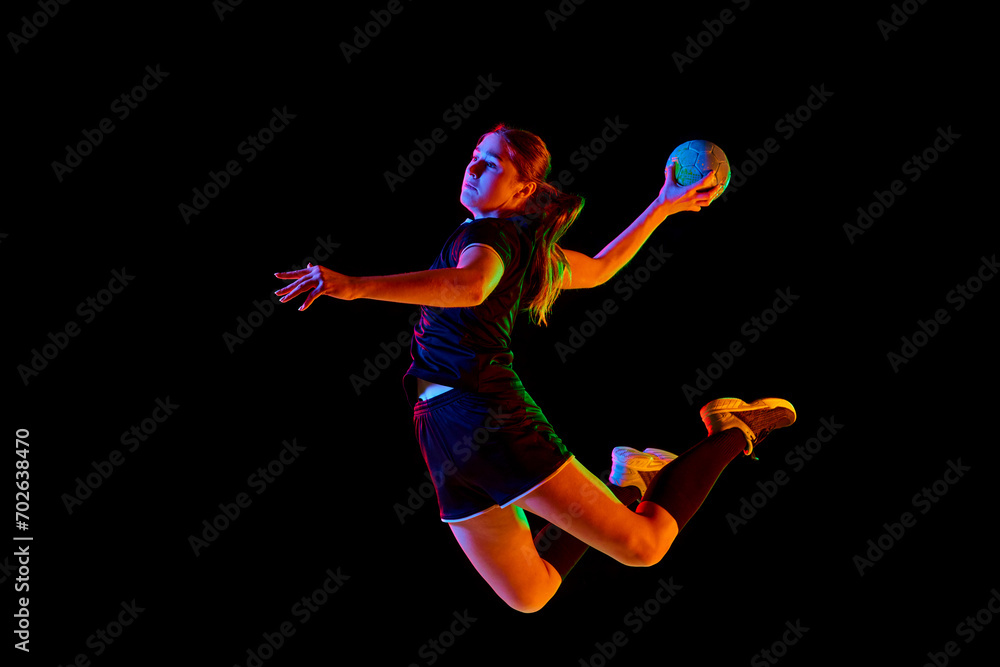 Fit, young, competitive female handball player demonstrating throwing techniques against black background in neon light. Concept of professional sport, movement, dynamic, workout, championship 2024