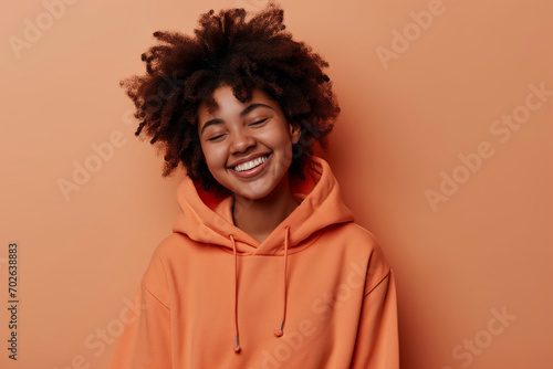 African American happy teenage girl wearing hoodie on peach background © Darya Lavinskaya