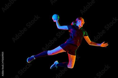 Fit, focused woman engaged in handball drills, displaying determination and focus against black background in mixed neon light. Concept of sport, hobby, movement, dynamic, championship, goal. Ad