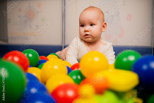 Cute baby girl playing with colorful balls in kindergarten.