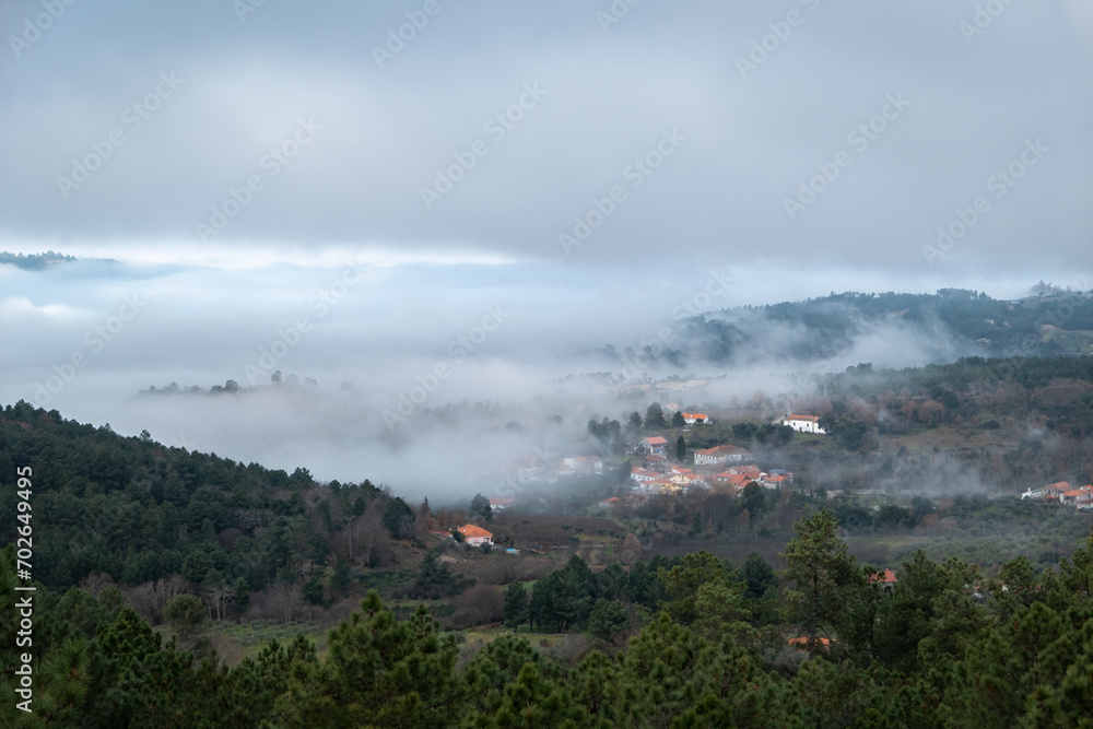 Aldeia rodeada por montanhas e floresta com o nevoeiro baixo a cobrir parte da floresta e da aldeia num dia frio de inverno Aldeia rodeada por montanhas e floresta com o nevoeiro baixo a cobrir parte da floresta e da aldeia num dia frio de inverno