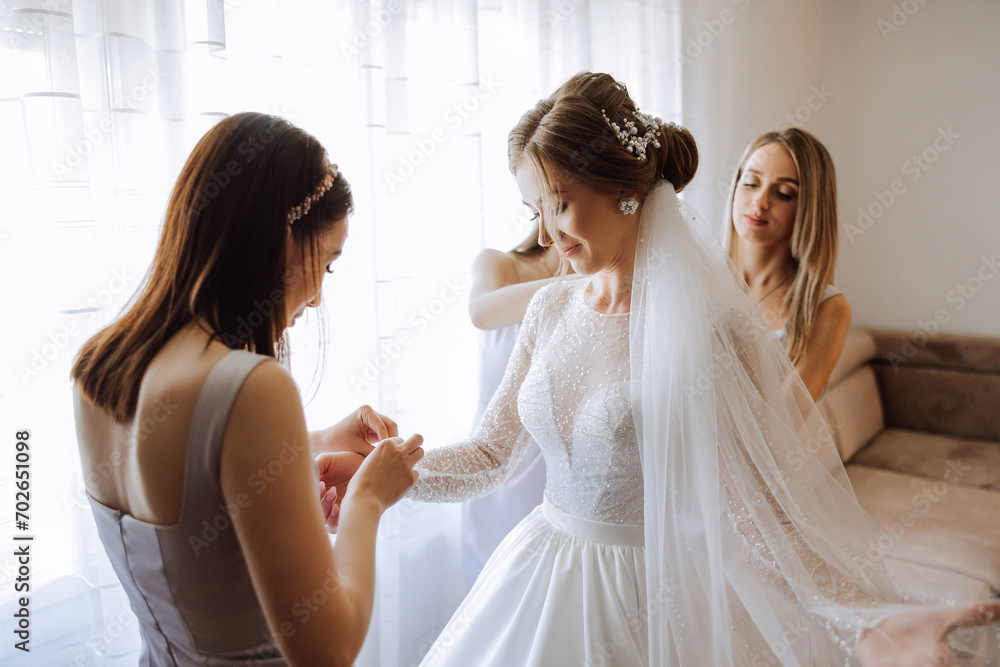 Naklejka premium Morning of the bride. The bride's maid of honor helps the bride lace up her dress, fasten buttons on the dress or sleeves. Girlfriends help the bride fasten her dress
