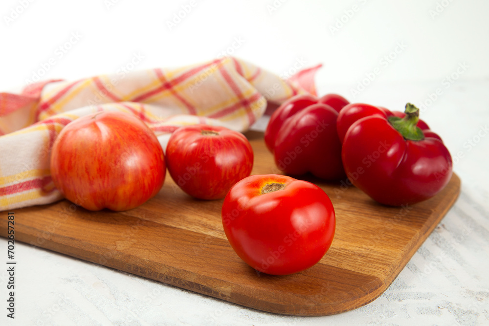 Cutting board with several red tomatoes and bell pepper on white wooden background with red kitchen towel.. Cutting board with several red tomatoes and bell pepper on white wooden background with red kitchen towel..