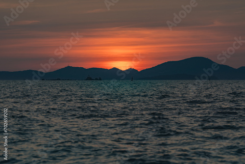 Beautiful golden sunset over the sea behind mountains in background and have light reflection on the water as the sunset. © Pornprasit Panada