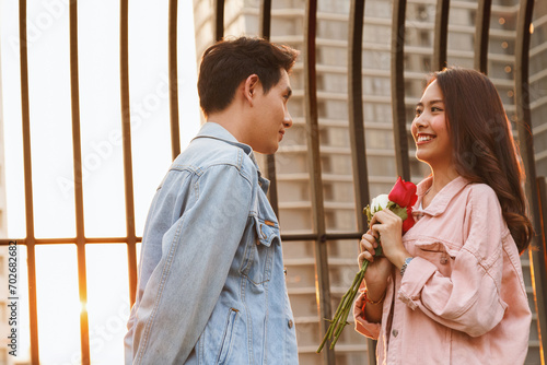 young happy couple love and romantic at first date relationship. asian teenage woman surprise and smiling at boyfriend gives red rose flowers at dinner in valentine day. couple and happiness concept.