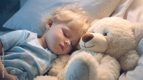 A little boy with blonde hair sleeps on a bed with a soft toy bear in her arms. A child's sweet sleep photo