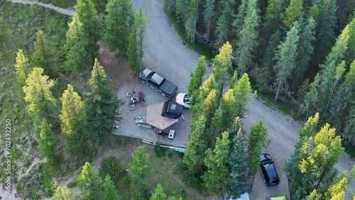 Birds eye view of a campsite with a rooftop tent setup and a couple vehicles surrounded by large pine trees photo