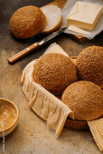 buns sprinkled with sesame seeds in a basket and a stick of butter, no people, brown background, close-up photo