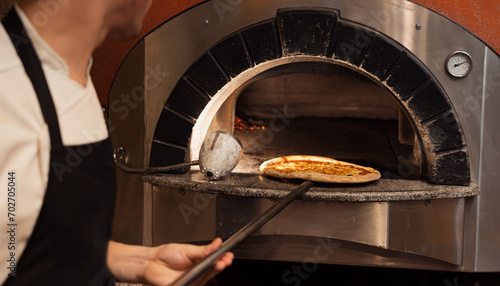A chef skillfully slides a pizza into a wood-fired oven, showcasing the blend of tradition and modern culinary techniques
