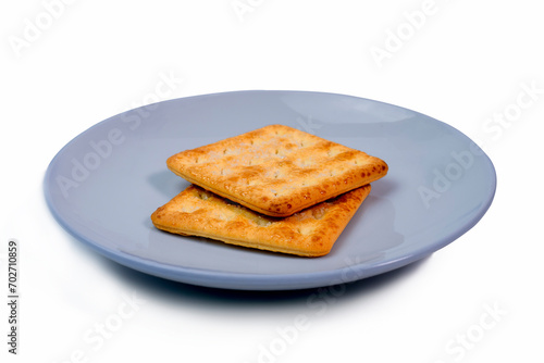 Two crackers placed on a small white ceramic plate. White background. Biscuits