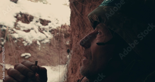 An elderly soldier sits with a machine gun in a trench, dugout and smokes. Military actions in the east of Ukraine 2023. Ukrainian-Russian war.