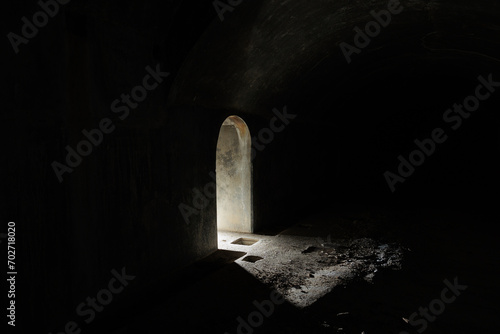 Vista degli interni totalmente oscuri di un ambiente interno ad una struttura abbandonata, con poca luce, con un corridoio illuminato lateralmente soltanto da una piccola luce artificiale photo