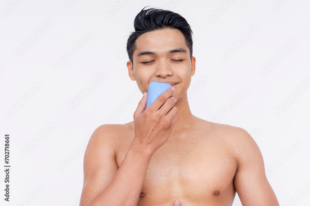 A young undressed asian man smelling the nice scent of a a deodorant soap. Isolated on a white backdrop.
