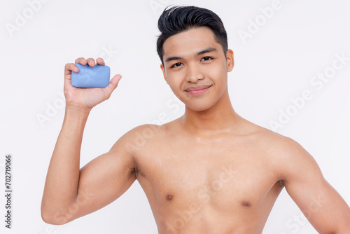 A young undressed asian man holding a blue bar of deodorant soap. Isolated on a white backdrop.