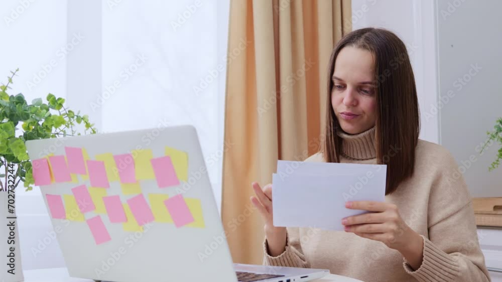 Casually dressed young woman holding papers in her hands calculating family budget trying to save some money having stressed and concentrated look paying bills Casually dressed young woman holding papers in her hands calculating family budget trying to save some money having stressed and concentrated look paying bills