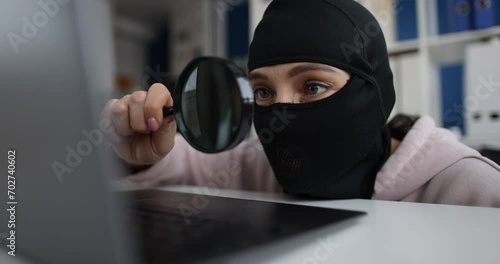 Internet theft and persons in balaclava with magnifying glass behind laptop. Internet intellectual property theft concept photo
