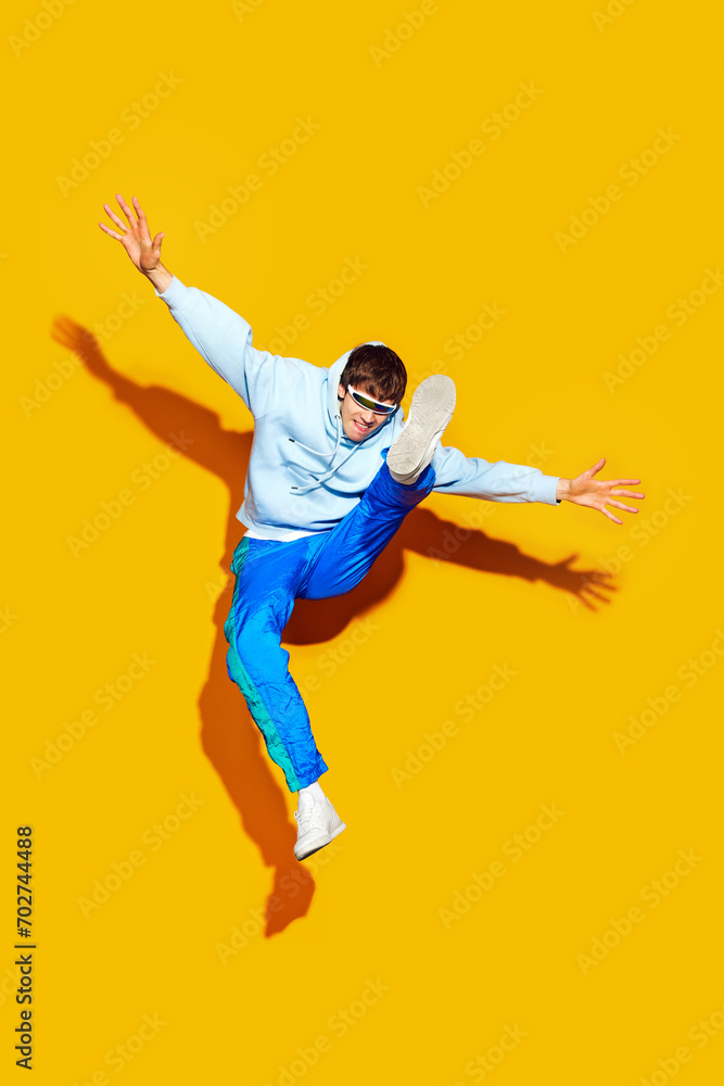 Trendy fashion in motion. Person jumps with flair, dressed stylish sportswear, shows pop of excitement against bright yellow background. Concept of beauty, trends, modern style, shopping, sales.