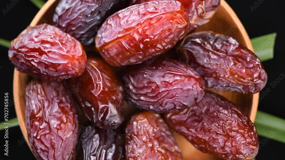 Dates fruit. Date fruits with palm tree leaf, in a wooden bowl, rotating on black background. Medjool dates close up. Top view Dates fruit. Date fruits with palm tree leaf, in a wooden bowl, rotating on black background. Medjool dates close up. Top view
