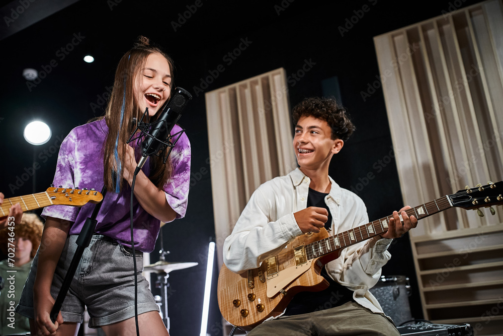 Fototapeta premium cheerful talented teenagers in casual outfits singing and playing guitars while in their studio