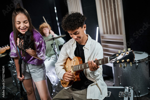 Fotografie cheerful cute teenage girl singing next to her cute friend playing guitar and ot