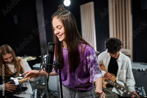 cheerful brunette teenage girl singing happily with her friends playing instruments in studio