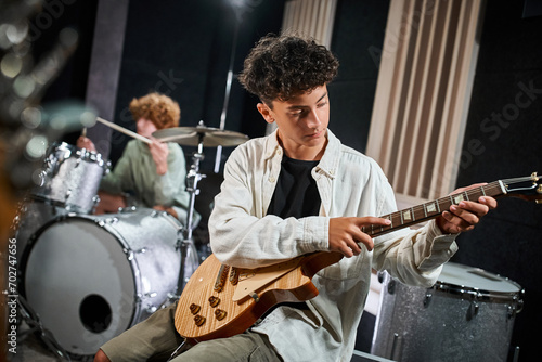 good looking talented teenage boy playing guitar next to his blurred drummer, musical group