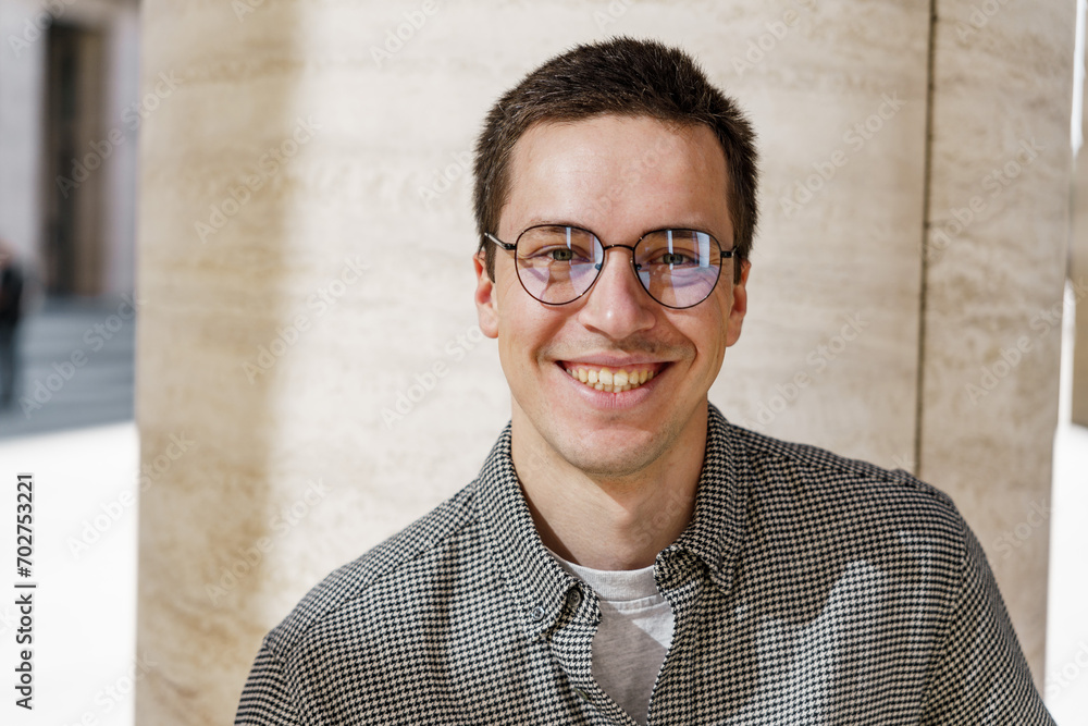 Smiling man with glasses in a houndstooth jacket standing against a textured wall, exuding casual confidence. Smiling man with glasses in a houndstooth jacket standing against a textured wall, exuding casual confidence.