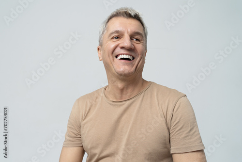 Cheerful mature man laughing heartily against a light background.