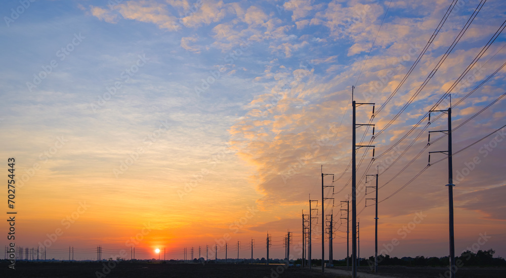 Silhouette two rows of many electric poles with cable lines on curve road in countryside area against beautiful sunset sky background, perspective widescreen view