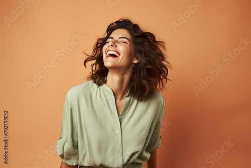 A woman laughing cheerfully in a light mint-green blouse against a soft peach background.