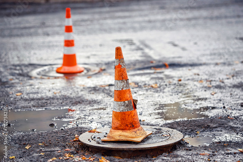 Orange traffic cone stands on manhole. Road repair works, asphalt laying, pylon to mark an obstacle or hole on road. Traffic cone stands on hatch, asphalt paving works photo
