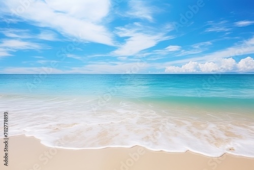  a sandy beach with waves coming in to the shore and a bright blue sky with white clouds in the background. © Shanti