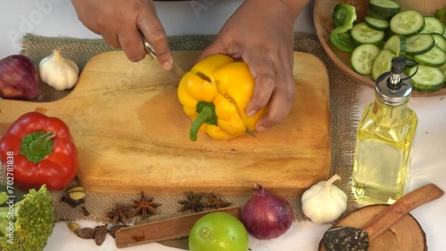 Close up shot of man cutting yellow bell pepper on wooden board