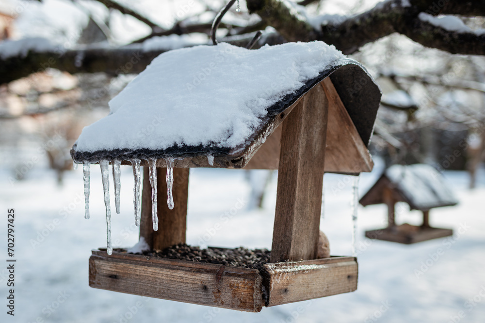 Wooden bird feeder with snow covered and frozen icicles hanging on a tree in winter Wooden bird feeder with snow covered and frozen icicles hanging on a tree in winter