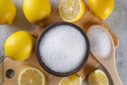 Foto Citric or lemon acid in clay bowl with a spoon, close-up, and whole ripe lemons on gray background