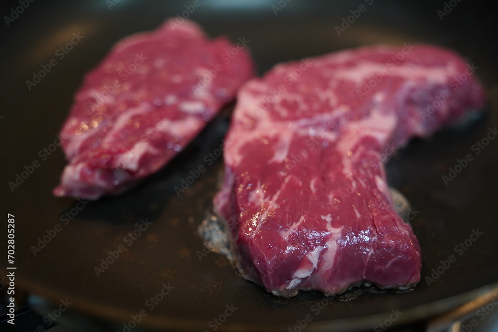 Place thick, fresh red raw beef on a heated frying pan to grill.