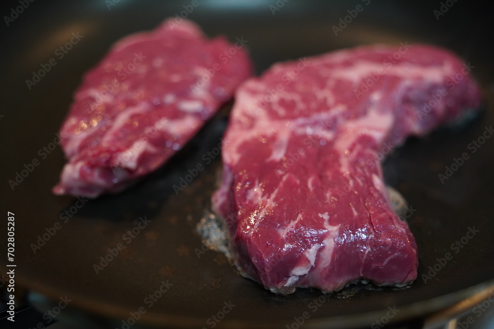 Place thick, fresh red raw beef on a heated frying pan to grill. Place thick, fresh red raw beef on a heated frying pan to grill.