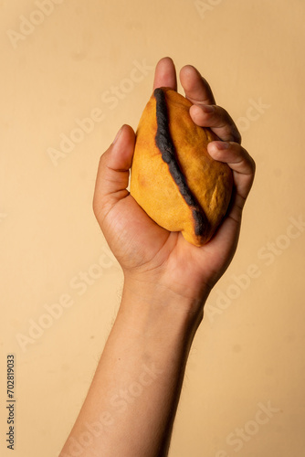 Salteña, empanada típica boliviana. Mano izquierda sosteniendo salteña en fondo color calido. photo