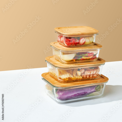 Glass food container with wooden lid filled with fruit, vegetable and protein. Plain cream and white colored background