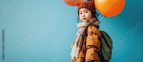 Little brunette asian child in oversized shirt dress brown beret and scarf boots She sending air kiss posing with multicolored balloons against blue background Fashion hipster style Full length photo