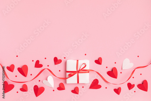 Valentine or mother day festive border with gift or present box and red hearts on pastel pink background top view. Flat lay greeting card.