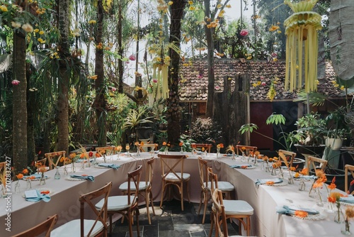 Fototapeta Naklejka Na Ścianę i Meble -  Arrangement decoration for intimate gathering with families or friends. Indonesian culture. Balinese, Javanese. Flower drops and hanging ornaments. Table setting. Long dinner table