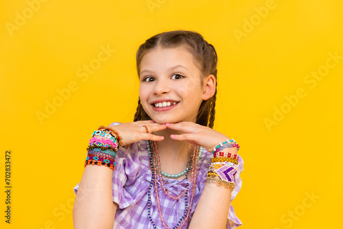 The young girl put on a lot of beaded jewelry. Beading for children and teenagers. Portrait of a little girl. Beaded bracelets. Yellow isolated background.