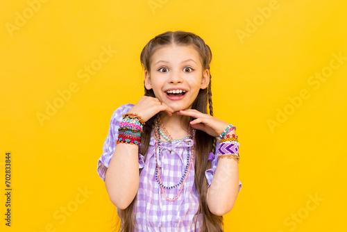 The child put on a lot of bracelets made of beads and beads. A happy little girl is enjoying a beaded ornament. Beading for children. Isolated yellow background.