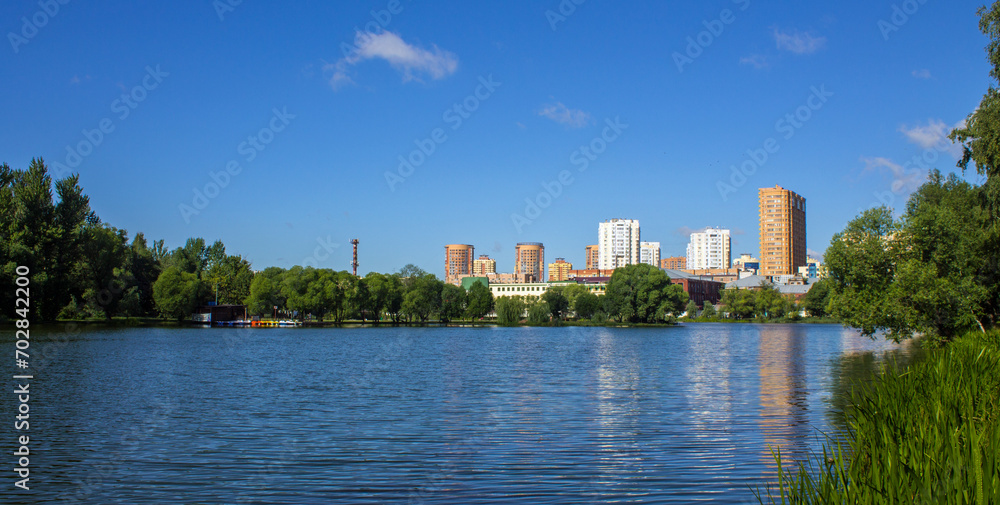 A modern residential area of the city of Reutov in the Moscow region on the shore of a pond with blue water and a city park on a sunny summer day and a space for copy