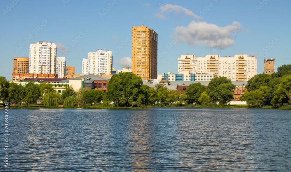 A modern residential area of the city of Reutov in the Moscow region on the shore of a pond with blue water and a city park on a sunny summer day and a space for copy A modern residential area of the city of Reutov in the Moscow region on the shore of a pond with blue water and a city park on a sunny summer day and a space for copy